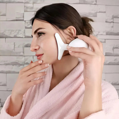 A woman in a pink bathrobe incorporating the Skin Revive LED face and neck massager into her daily at-home skincare routine for lymphatic drainage.