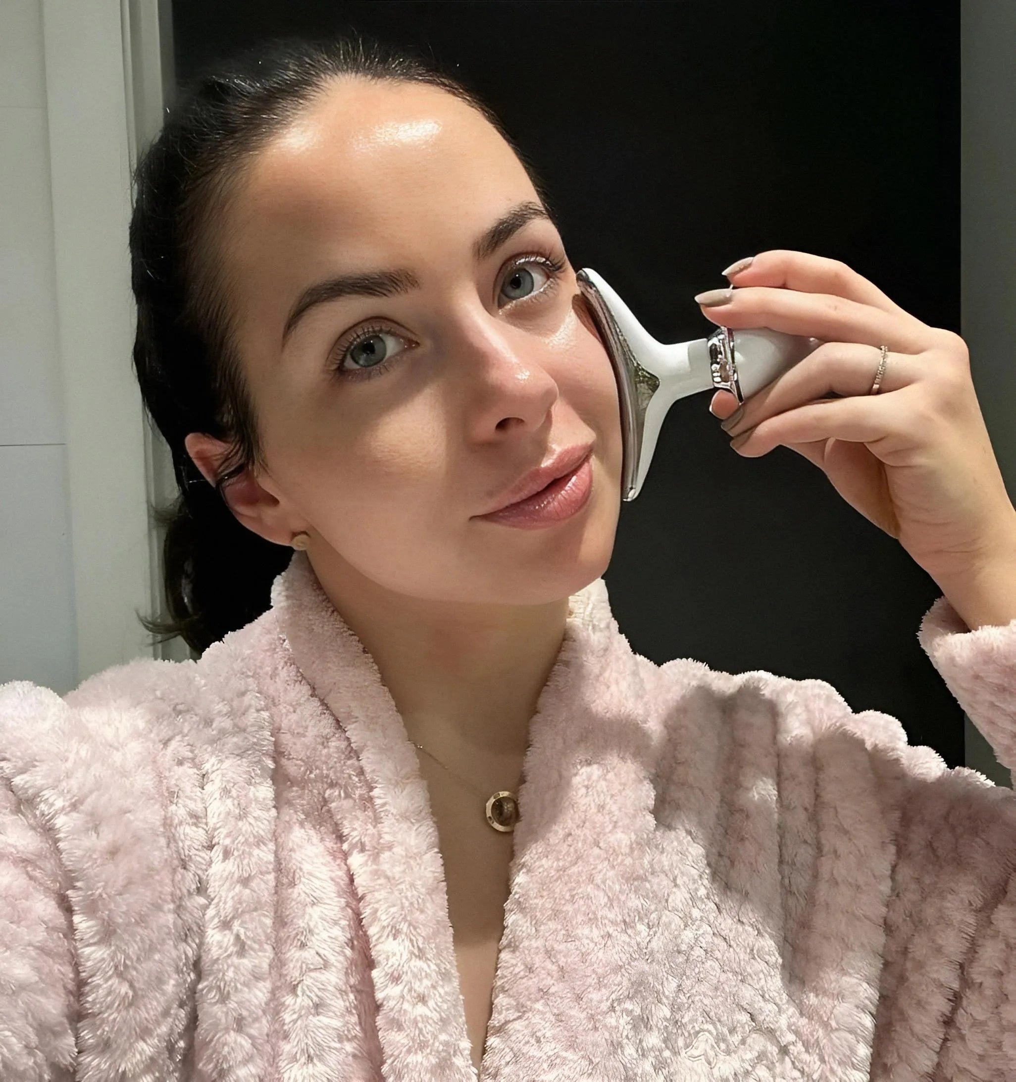 A woman in a pink robe enjoying her 5-minute morning skincare routine with the Skin Revive LED face massager.