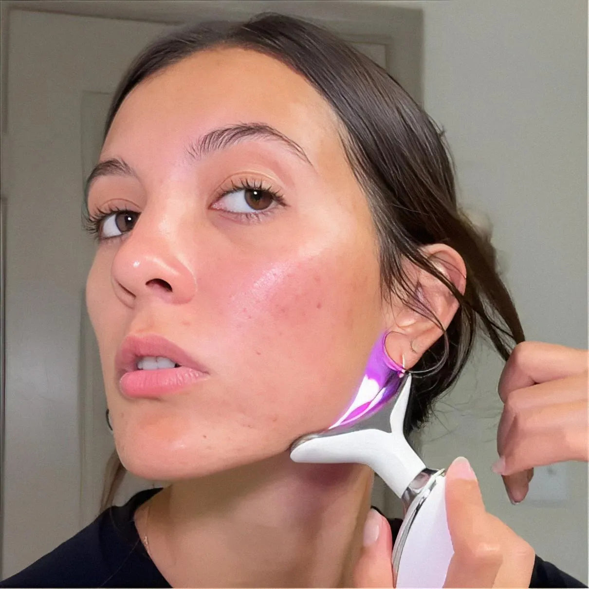 A customer demonstrating the purple LED light setting on the Skin Revive massager to assist with lymphatic drainage and de-puffing.
